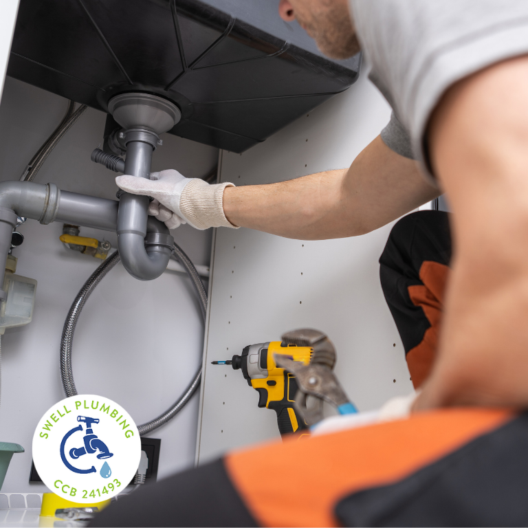 Plumber inspecting under-sink drain pipes in a Salem, OR home, checking for leaks and preparing plumbing for fall maintenance.