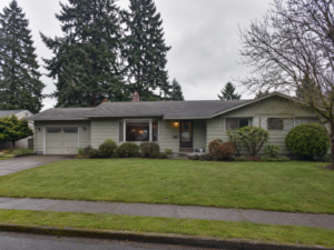 Photorealistic exterior of a modest post-1950s ranch-style home in Salem, Oregon, with muted siding, a low roofline, attached garage, mature evergreen trees, damp sidewalk, and a green front lawn on an overcast Pacific Northwest day.