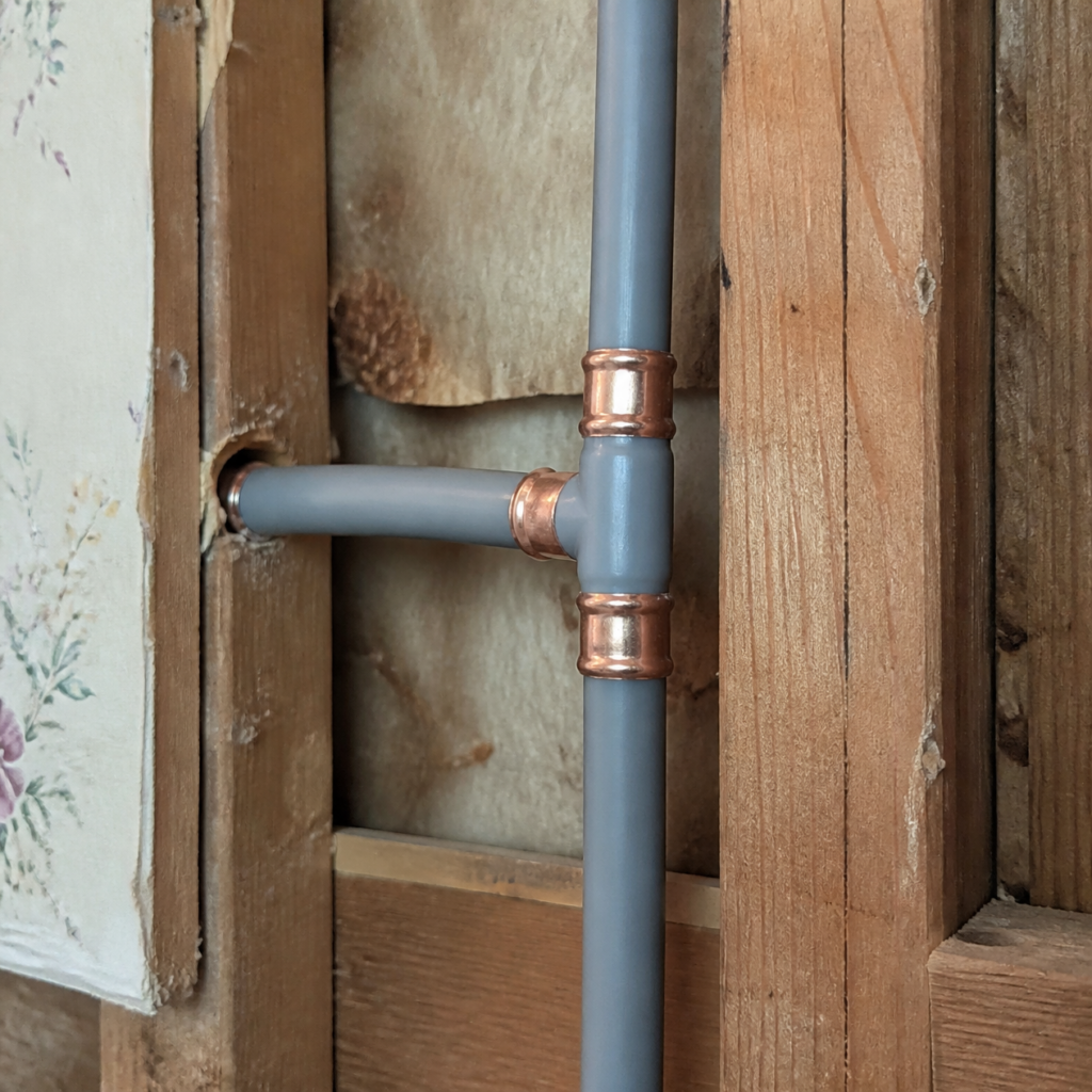 Gray polybutylene supply pipe with copper crimp rings in an open wall